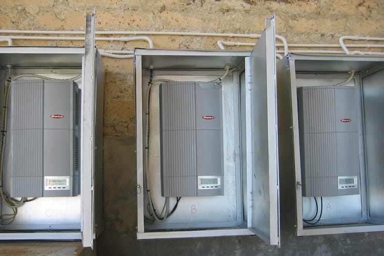 Trzy inwertery solarne w metalowych szafkach podłączonych do ściany.